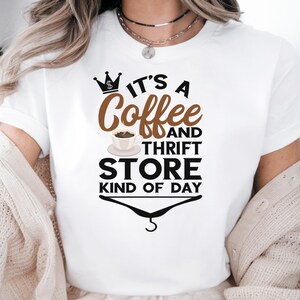 May include: White t-shirt with a brown and black graphic that says "It's a Coffee and Thrift Store Kind of Day". The graphic includes a crown with a dollar sign, a cup of coffee, and a hanger.