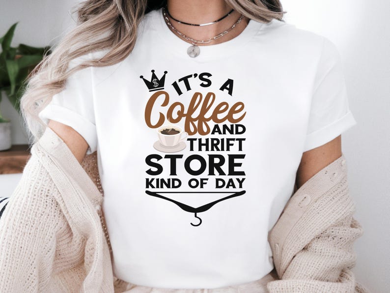 May include: White t-shirt with a brown and black graphic that says "It's a Coffee and Thrift Store Kind of Day". The graphic includes a crown with a dollar sign, a cup of coffee, and a hanger.