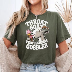 May include: A green t-shirt with a white graphic of a goat eating ice cream. The text on the shirt reads "Throat Goat Professional Gobbler".