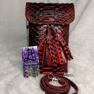 May include: A red and black snakeskin-textured crossbody bag with a flap closure and a matching tassel. The bag includes a detachable strap and a tag that reads "Authentic by deDenio".