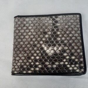 May include: A bi-fold wallet with a snakeskin pattern in shades of gray and black. The wallet has a black border and a textured surface. The wallet is rectangular and appears to be made of leather.