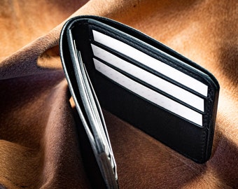 May include: A black leather wallet with multiple card slots and a billfold. The wallet is open and lying on a brown fabric surface.