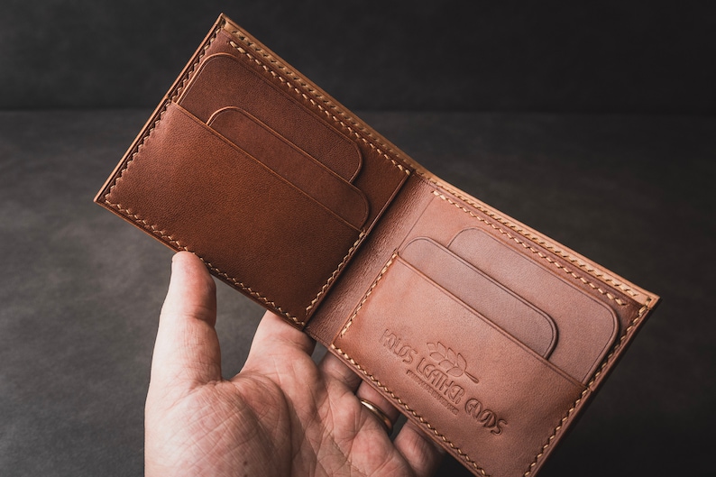 May include: A brown leather wallet with multiple card slots and a stitched edge. The wallet is open and the inside is visible, showing a brand logo that reads "Rus Leather Goods".