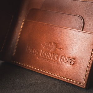 May include: A brown leather wallet with multiple card slots and a stitched edge. The wallet has the text "Roots Leather Goods" embossed on the front.