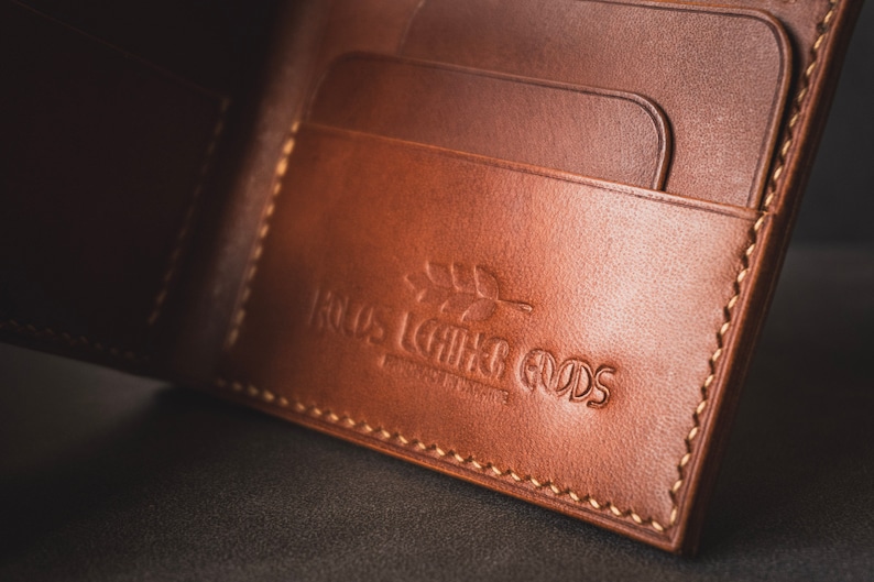 May include: A brown leather wallet with multiple card slots and a stitched edge. The wallet has the text "Roots Leather Goods" embossed on the front.