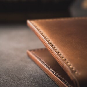 May include: Close-up of a brown leather wallet with stitching detail. The wallet is folded in half and the stitching is visible on the edge.