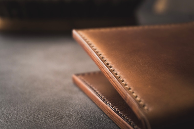 May include: Close-up of a brown leather wallet with stitching detail. The wallet is folded in half and the stitching is visible on the edge.