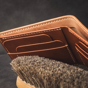 May include: A brown leather wallet with multiple card slots and a billfold. The wallet is open and the interior is visible.