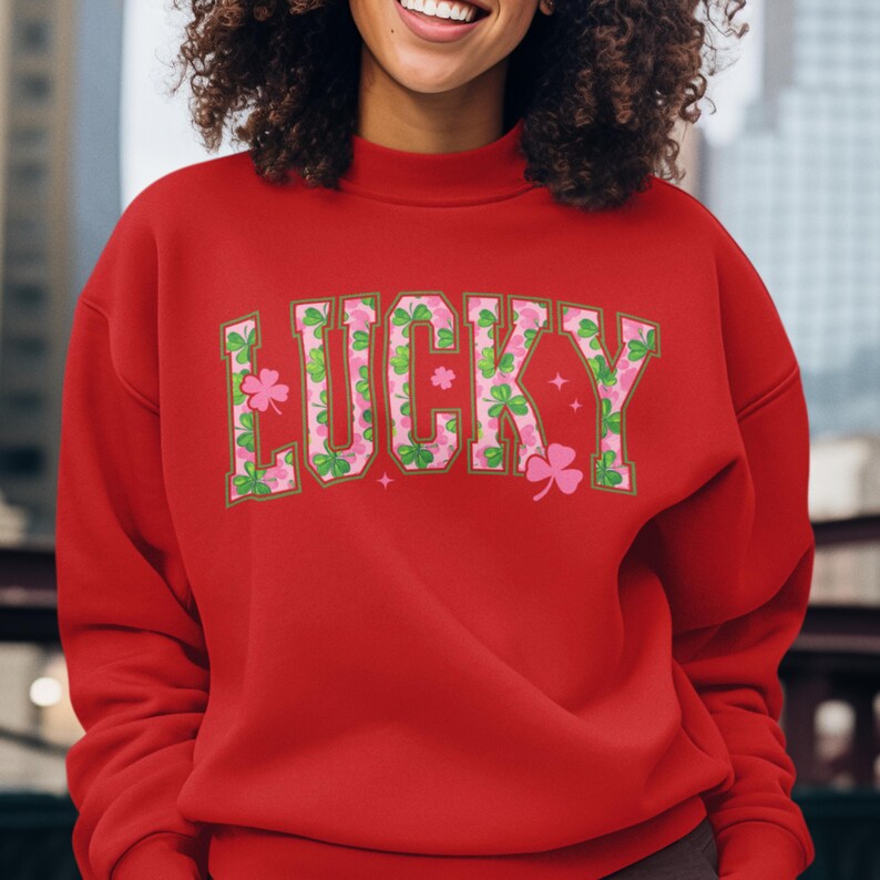 May include: A red sweatshirt with the word "LUCKY" in a green and pink floral pattern. The letters are outlined in a darker green. The sweatshirt has a crew neck and long sleeves.