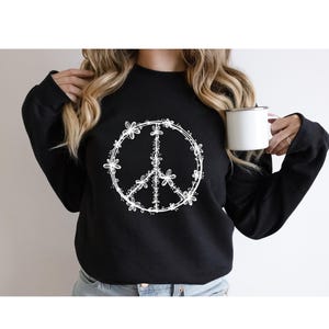 May include: Black sweatshirt with a white peace sign design made of flowers.
