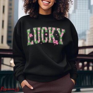 May include: Black sweatshirt with the word "LUCKY" in green and pink lettering. The letters are decorated with shamrocks and floral patterns. The sweatshirt is a crew neck style.