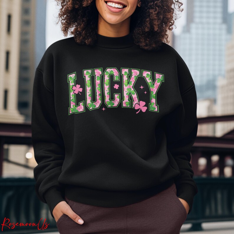 May include: Black sweatshirt with the word "LUCKY" in green and pink lettering. The letters are decorated with shamrocks and floral patterns. The sweatshirt is a crew neck style.