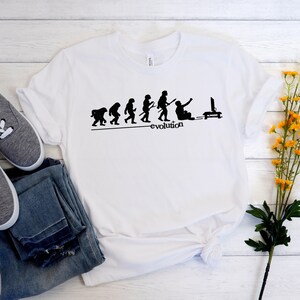 May include: White t-shirt with a black silhouette of the evolution of man, ending with a man sitting in front of a computer screen. The text "evolution" is below the silhouettes.