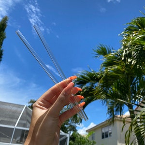May include: Two clear glass drinking straws held in a hand against a blue sky background.