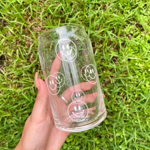 May include: A clear glass can with a white smiley face design. The can has the words "Smile Today" printed on the bottom.