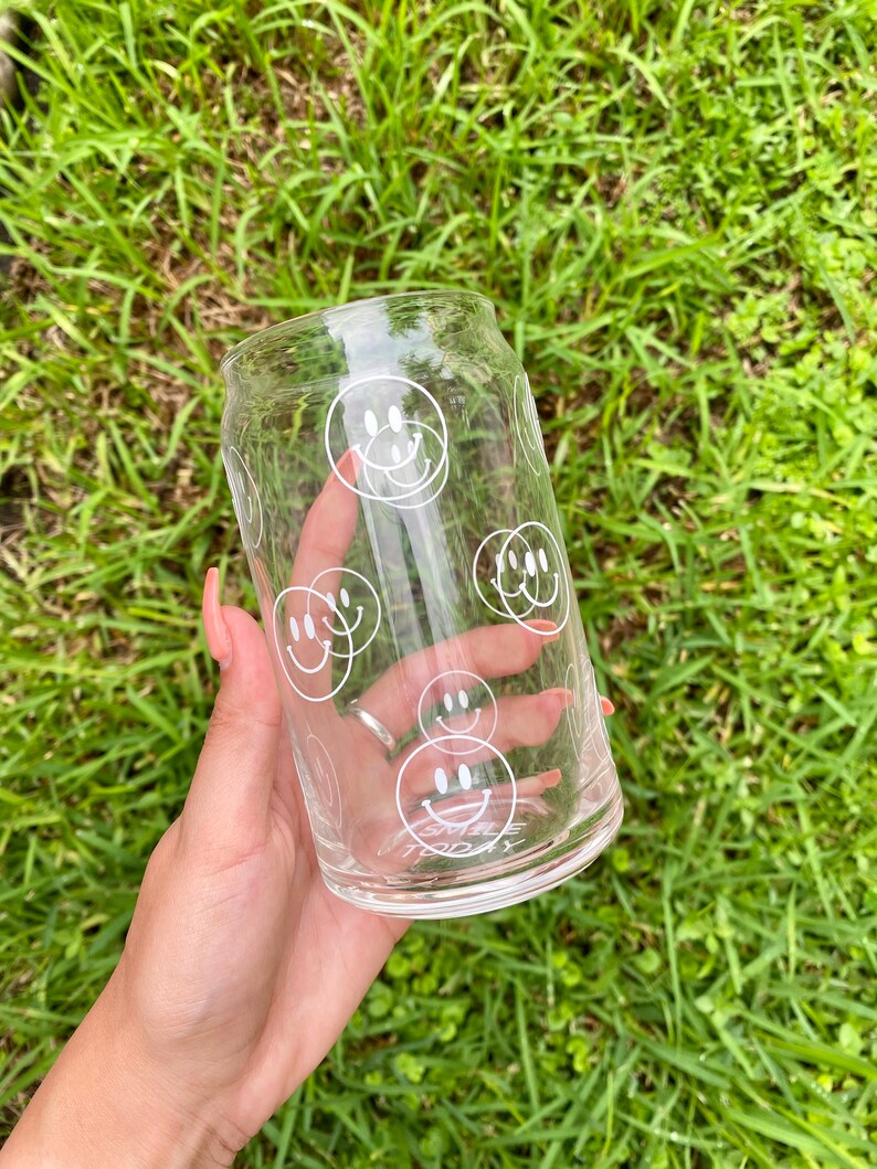 May include: A clear glass can with a white smiley face design. The can has the words "Smile Today" printed on the bottom.