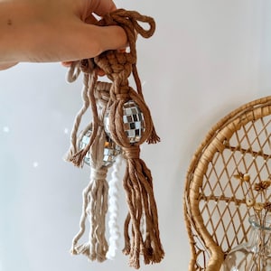 May include: Two brown and beige macrame tassels with silver disco ball ornaments attached. The tassels are hanging from a white background.