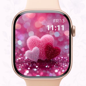May include: A gold smartwatch with a pink heart-themed display. The screen shows three heart shapes in varying shades of pink and red against a glittery background. The time reads 11:11 on Friday the 13th.