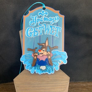 Puede incluir: Un adorno azul y marrón con un reno de dibujos animados y el texto "You may get wet".