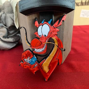 May include: A red and gold 3D printed dragon figurine with a blue and white bird in its mouth. The dragon has a wide, toothy grin and large, round eyes.