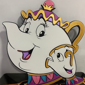 Puede incluir: Una tetera blanca con una tapa morada y ribetes dorados, con una taza de té blanca más pequeña con un asa dorada y una cara sonriente. La tetera tiene una cara grande y sonriente con labios morados y pestañas.