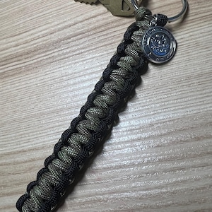 May include: A black and green paracord keychain with a silver key ring and a silver charm with the United States Seal.