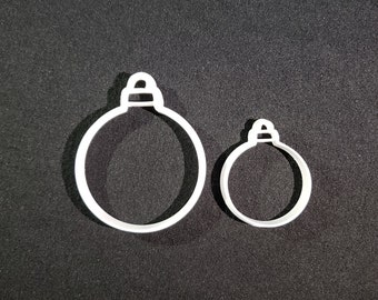 May include: Two white plastic Christmas ornament cookie cutters. The larger cutter is about 2 inches in diameter and the smaller cutter is about 1 inch in diameter.