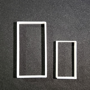 May include: Two white plastic cookie cutters in the shape of rectangles. The larger rectangle is about twice the size of the smaller rectangle.