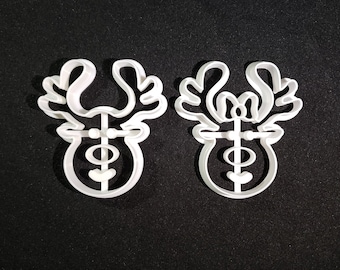 May include: Two white plastic reindeer cookie cutters. The reindeer have a simple design with antlers, a nose, and eyes.