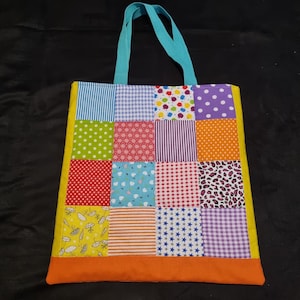 May include: A colourful patchwork tote bag with a turquoise handle. The bag is made of different fabrics with various patterns, including polka dots, stripes, and flowers. The bag has a yellow border and an orange bottom.