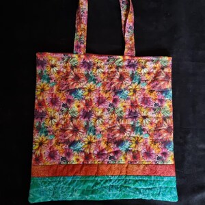 May include: A quilted tote bag with a floral print in shades of pink, orange, yellow, and green. The bag has a turquoise and orange trim.