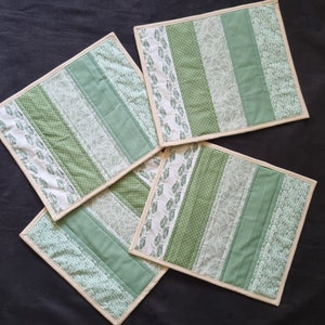 May include: Four green and white striped fabric coasters with a cream border. The coasters are arranged in a square shape.