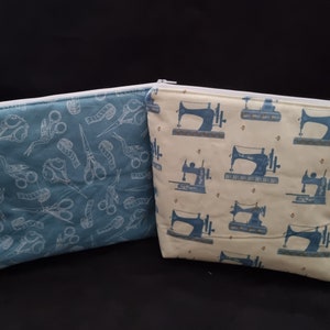 May include: Two zippered pouches, one with a blue background and a white pattern of scissors, spools of thread, and birds, and the other with a cream background and a blue pattern of sewing machines.