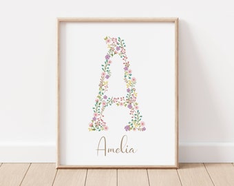 Puede incluir: Un arte de pared con estampado floral que presenta la letra A con el nombre Amelia escrito debajo. La letra está compuesta por flores rosas, moradas y verdes.