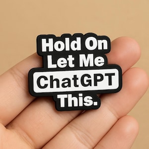 May include: A black and white rectangular pin with the text "Hold On Let Me ChatGPT This." The pin has a black border and white lettering. The pin is held in a hand.