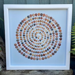 May include: A white framed picture with a light blue background featuring a spiral design made of small, colourful seashells.