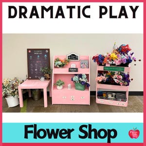 Peut inclure: Un ensemble de jeu de boutique de fleurs rose avec une liste de prix sur un tableau noir, un présentoir à deux étagères et un chariot roulant à trois étagères. Les étagères sont remplies de fleurs artificielles colorées. Le panneau au-dessus de la boutique indique "Flower Shop".