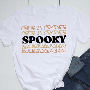 May include: White t-shirt with the text "SPOOKY" in black letters, surrounded by orange and yellow outlines. The outlines are repeated above and below the word "SPOOKY".