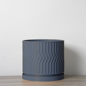May include: A dark gray ceramic planter with a geometric pattern and a matching saucer. The planter is empty and sitting on a wooden surface.