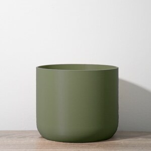 Peut inclure: Un pot de fleurs cylindrique vert mat. Le pot est fait d'un matériau lisse et solide.