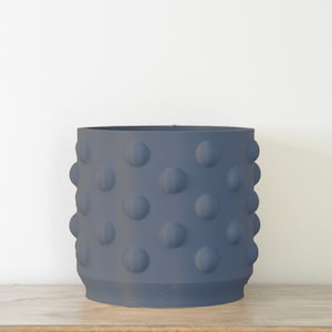 Puede incluir: Un macetero de cerámica azul oscuro con una superficie texturizada y punteada. El macetero es redondo y tiene una abertura ancha.