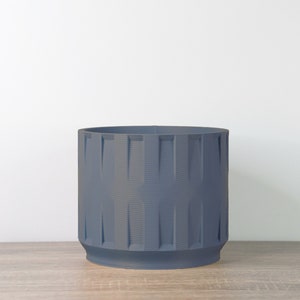May include: A dark gray cylindrical planter with a textured, ribbed design. The planter is made of a durable material and has a modern, minimalist aesthetic.
