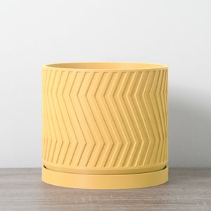 May include: A yellow planter with a chevron pattern. The planter has a matching saucer.
