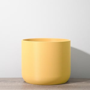 May include: A yellow ceramic planter with a rounded bottom and a smooth, matte finish.