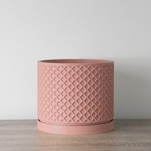 May include: A dusty rose planter with a geometric diamond pattern. The planter has a matching saucer.