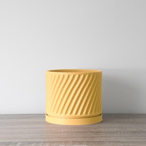 May include: A yellow ceramic planter with a swirl design and a matching saucer. The planter is sitting on a wooden surface.