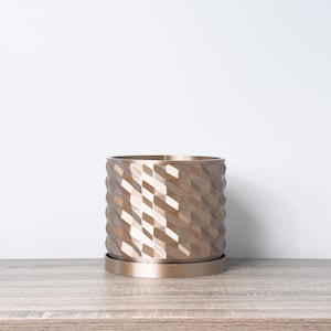 May include: A gold-coloured geometric planter with a textured surface. The planter has a matching saucer.