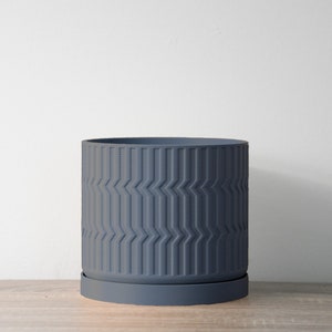 May include: A dark gray planter with a geometric pattern. The planter has a matching saucer.