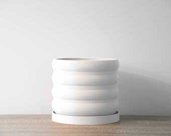 May include: White ceramic planter with a wavy, ridged design and a matching saucer. The planter is empty.