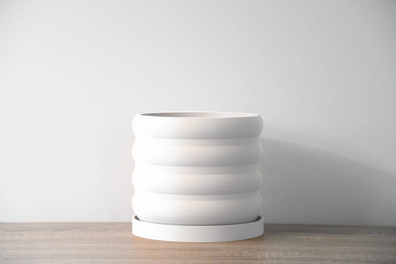 May include: White ceramic planter with a wavy, ridged design and a matching saucer. The planter is empty.